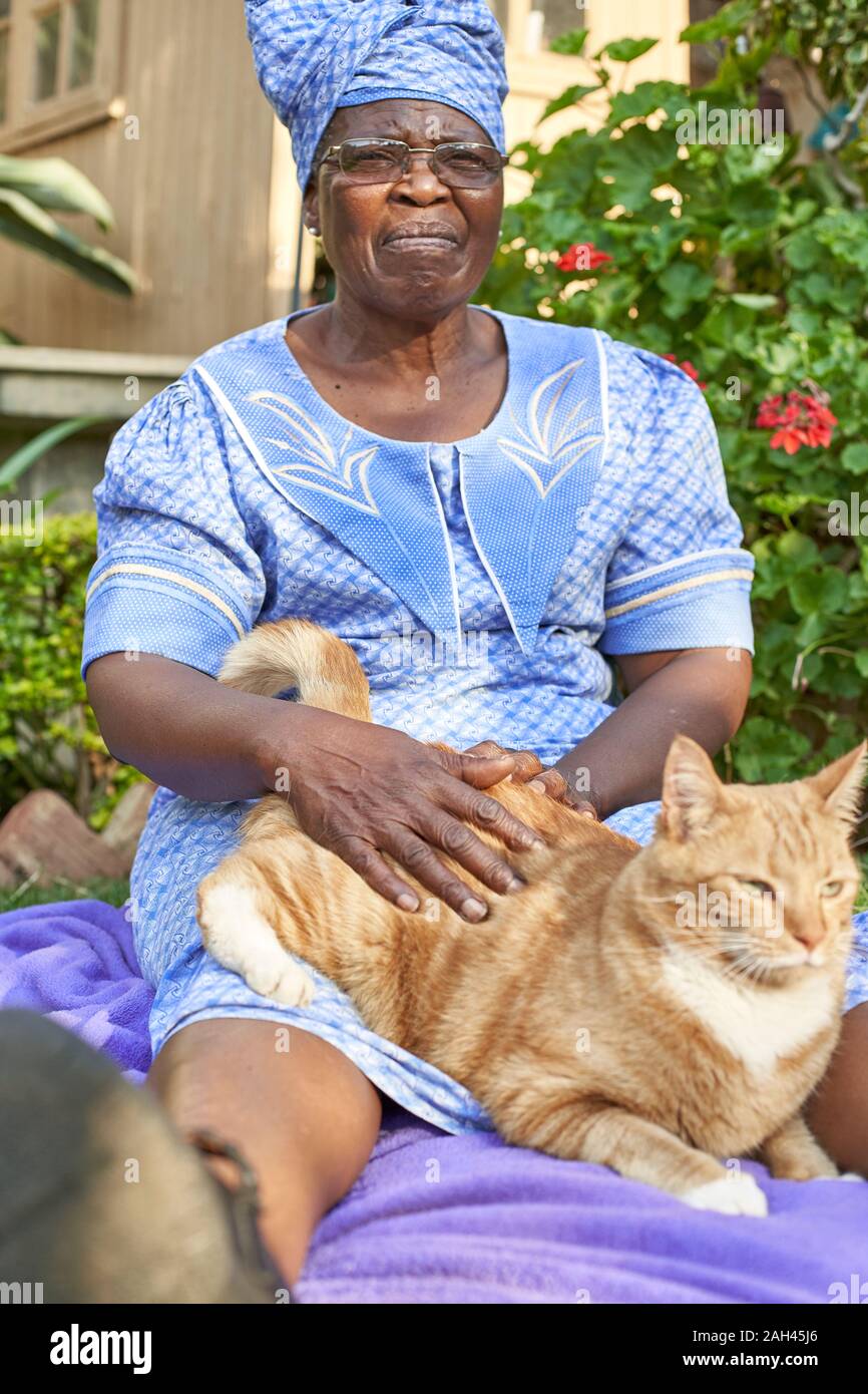 Ältere Frau mit einer Katze sitzt auf einer Decke im Garten Stockfoto