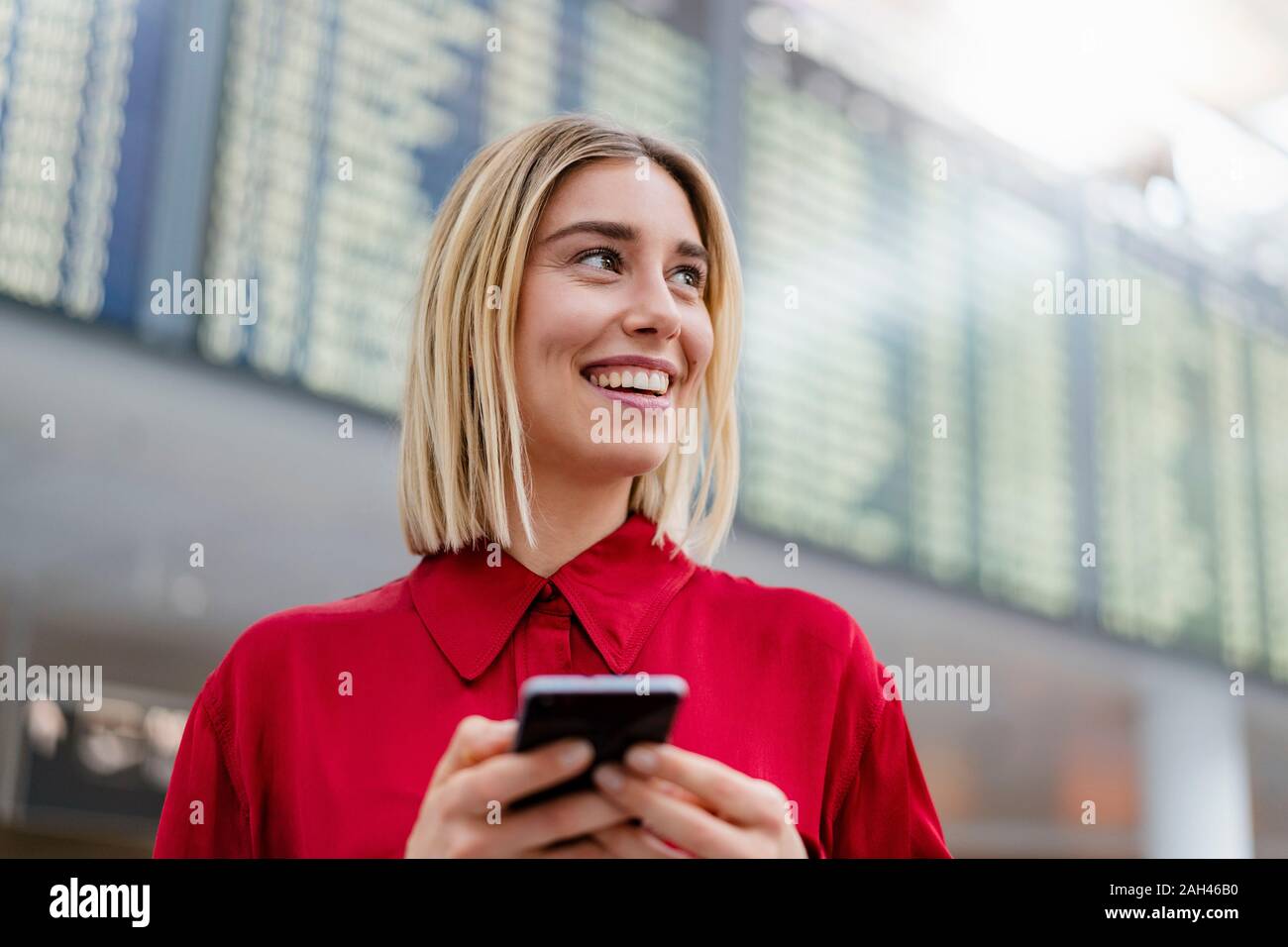 Lächelnden jungen Geschäftsfrau mit Mobiltelefon bei Ankunft Abflug am Flughafen Stockfoto