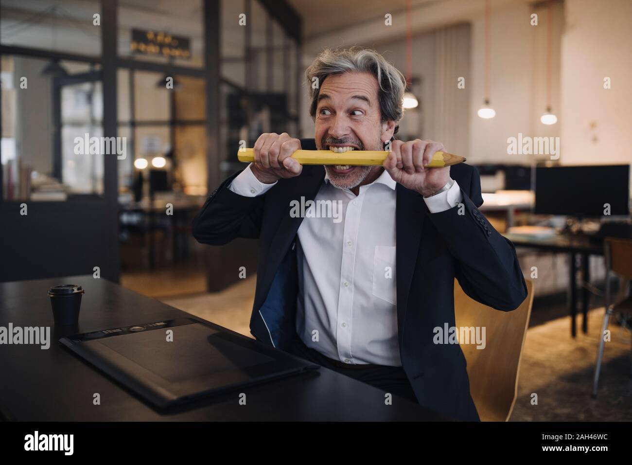 Wütend älterer Geschäftsmann mit riesigen Bleistift am Schreibtisch im Büro Stockfoto