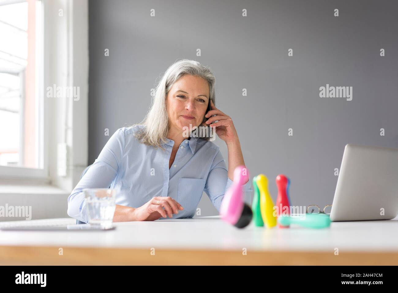 Reife Geschäftsfrau auf dem Handy Spielen mit Stiften auf dem Schreibtisch im Büro Stockfoto