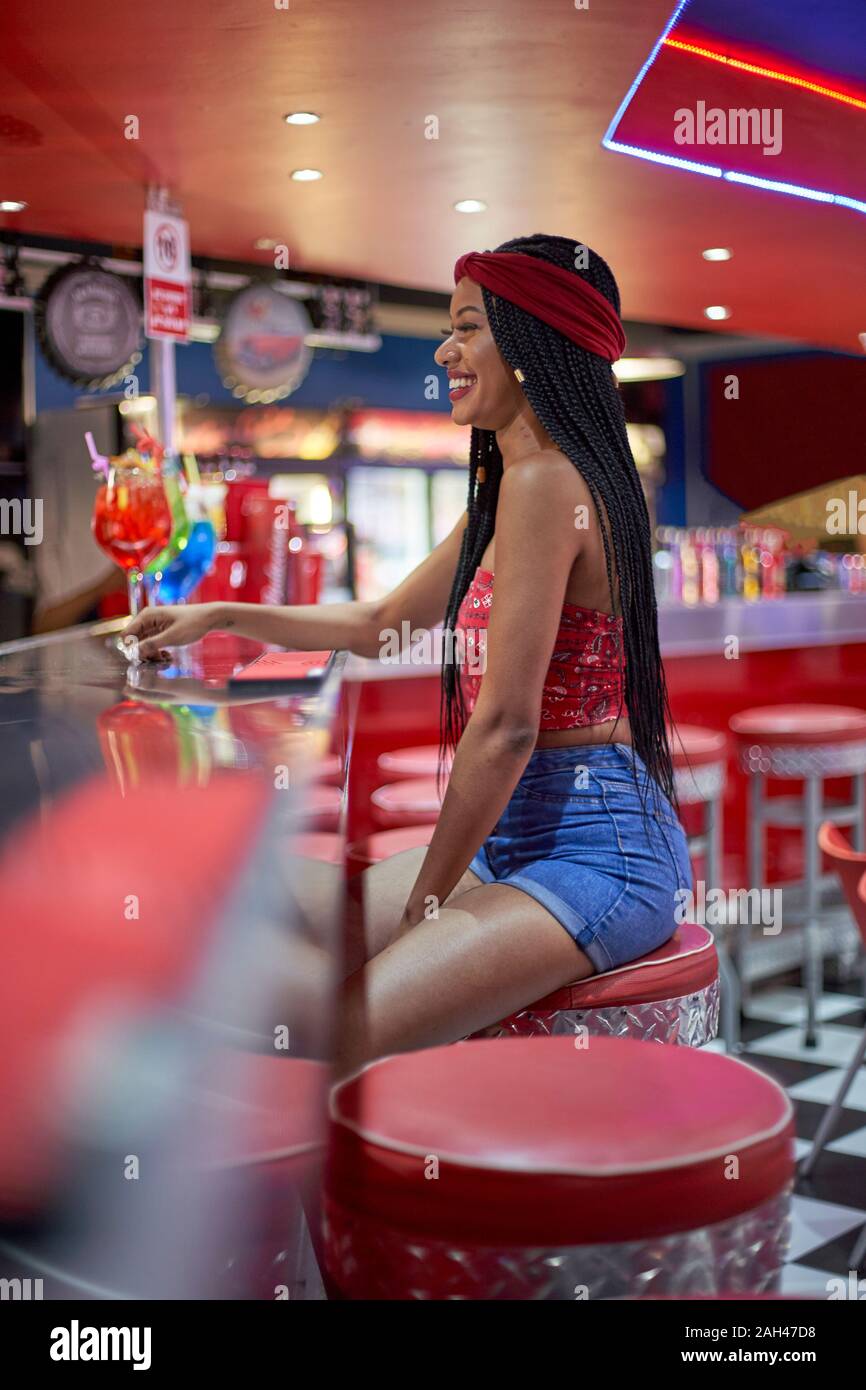 Junge Frau mit geflochtenem Frisur sitzt auf einem Restaurant Bar Red Hocker Stockfoto