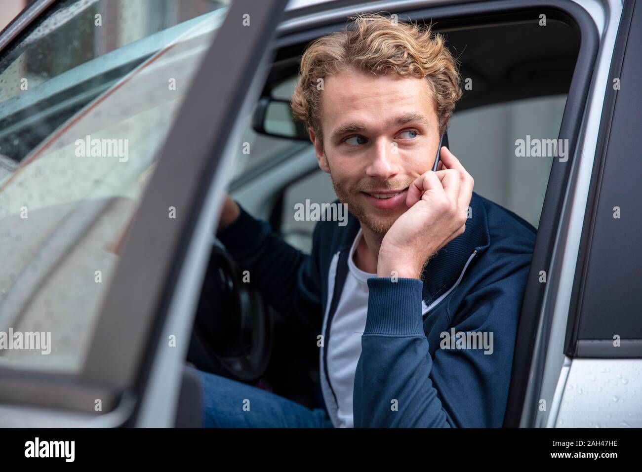 Junger Mann telefonieren und Sitzen im Auto, seitlich auf der Suche Stockfoto