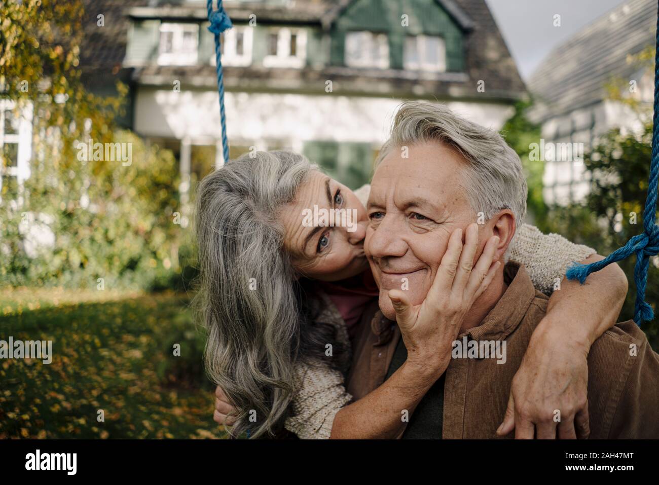 Glückliche Frau umarmen, küssen ein älterer Mann auf einer Schaukel im Garten Stockfoto