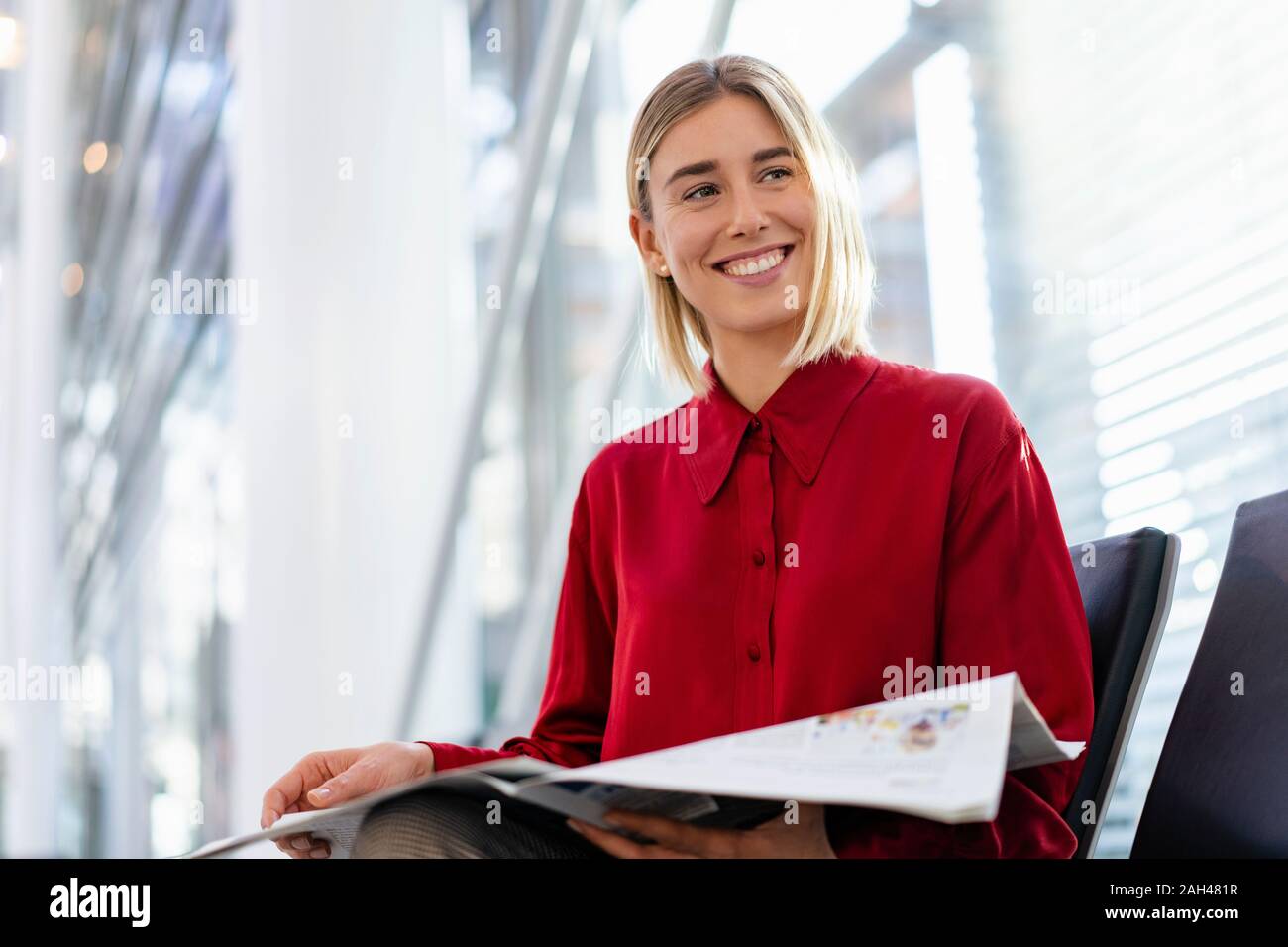 Lächelnden jungen Geschäftsfrau mit Zeitung sitzen im Wartebereich Stockfoto