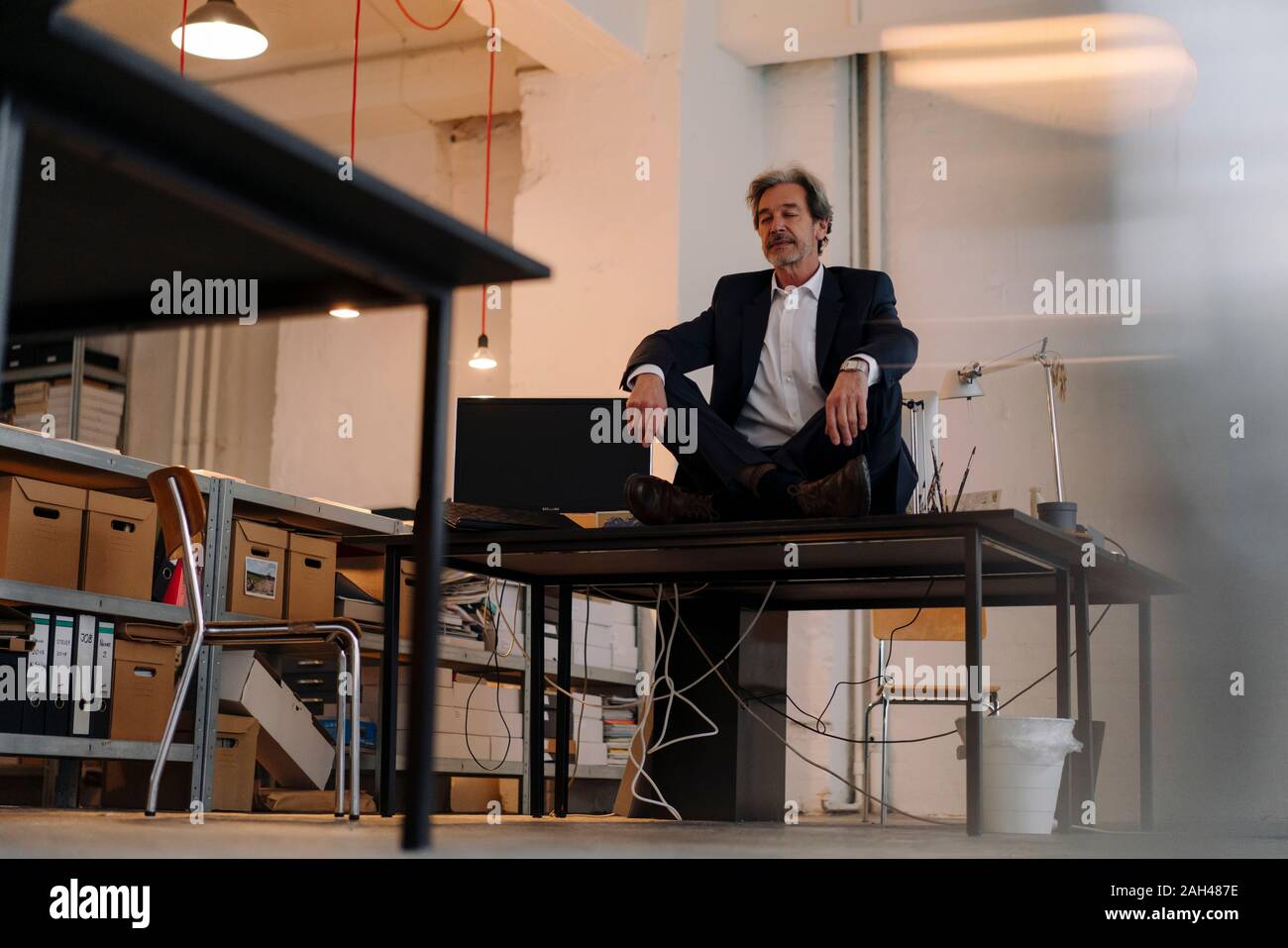 Senior Geschäftsmann mit überkreuzten Beinen auf dem Schreibtisch im Büro meditieren Stockfoto