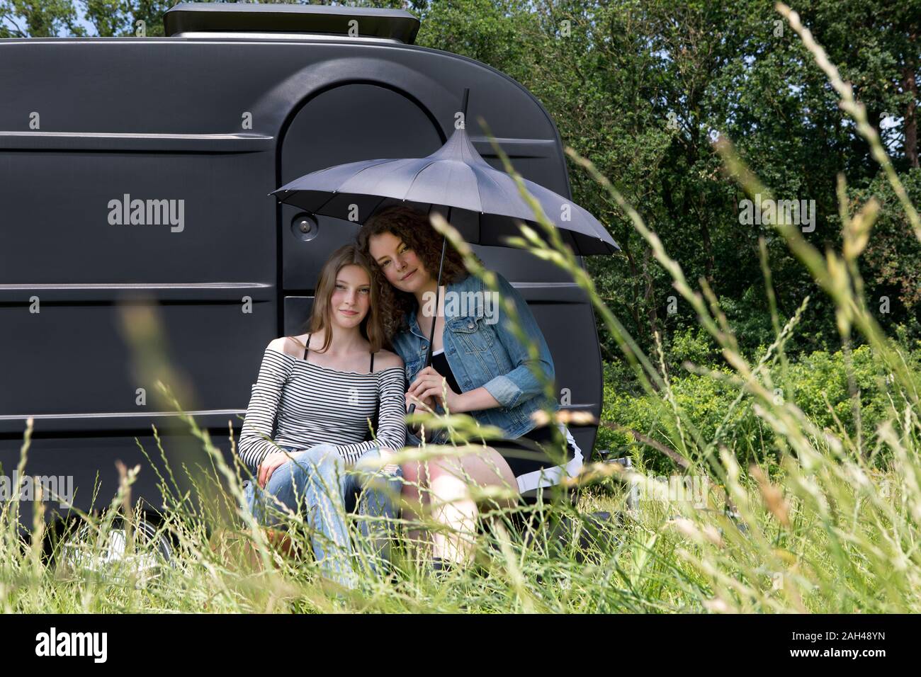 Porträt von zwei beste Freunde mit Regenschirm sitzen auf einer Wiese vor der schwarzen Caravan Stockfoto