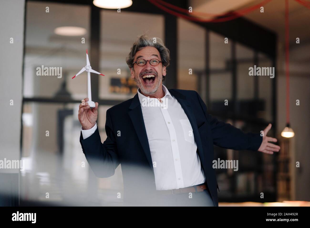 Aufgeregt älterer Geschäftsmann mit wind turbine Modell im Büro Stockfoto