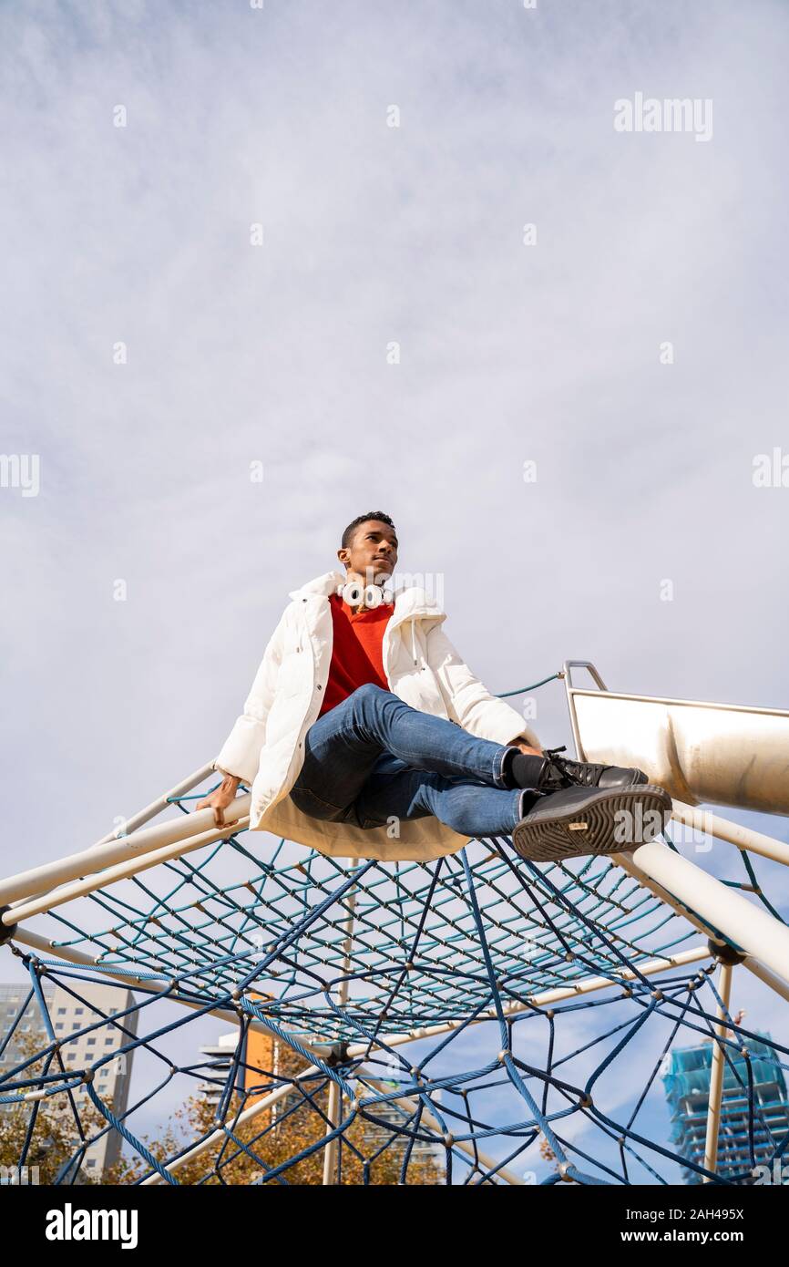 Junge Mann sitzt auf einem Klettergerüst auf dem Spielplatz Stockfoto