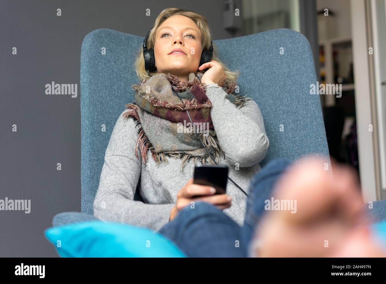 Junge Frau im Sessel sitzen, Musik hören mit Kopfhörern Stockfoto