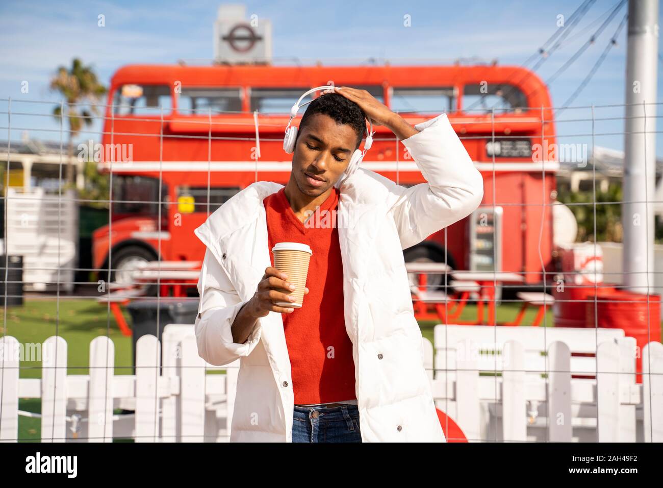 Stilvolle junger Mann mit Kopfhörern und Kaffee zum Mitnehmen im Freien Stockfoto