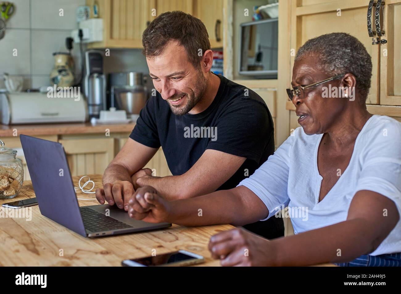 Ältere Frau und lächelnden Mann am Küchentisch sharing Laptop Stockfoto