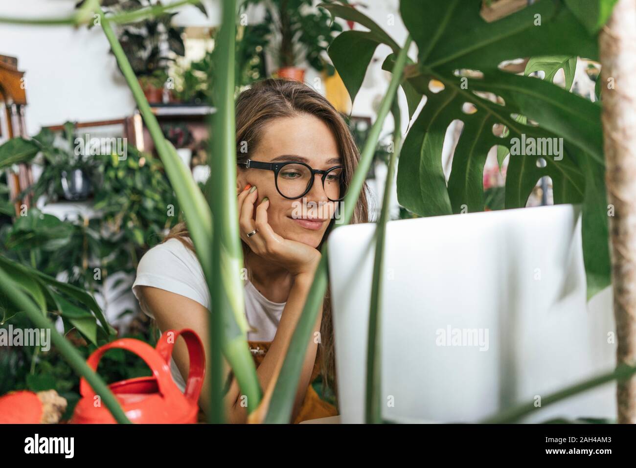 Junge Frau mit Laptop, umgeben von Pflanzen Stockfoto