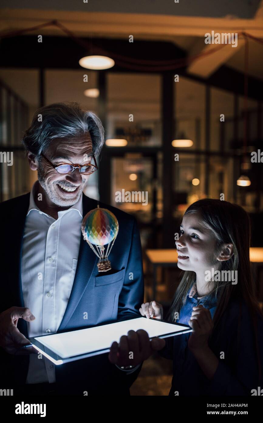 Happy senior buisinessman und Mädchen mit Heißluft-Ballon und glänzende Tablette im Büro Stockfoto