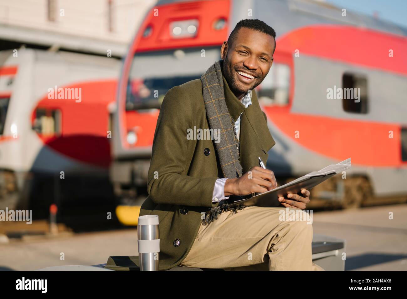 Portrait von Happy Geschäftsmann mit wiederverwendbaren Cup und Dokumente warten auf den Zug Stockfoto