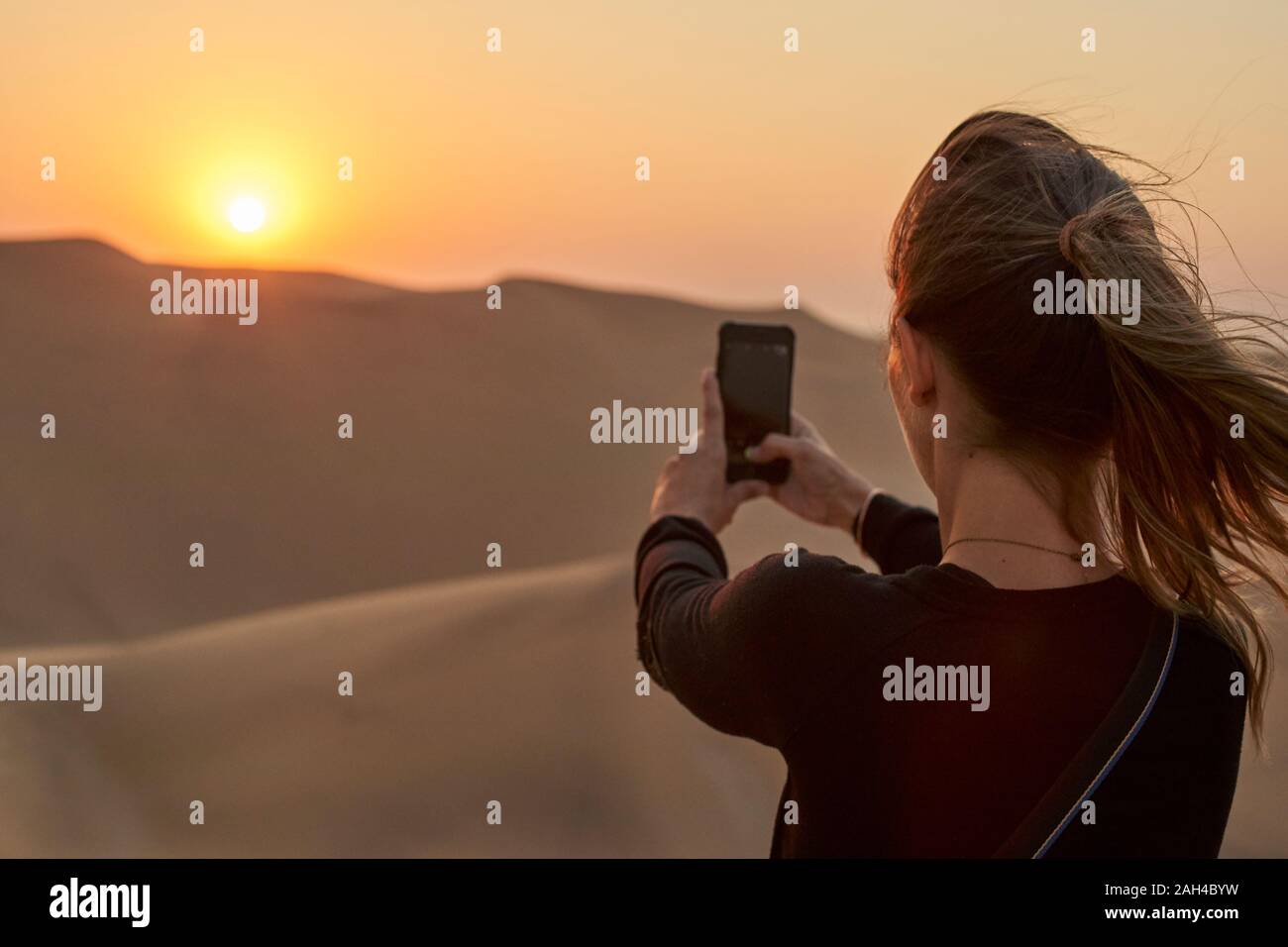Frau, die ein Smartphone Bild in der Wüste bei Sonnenuntergang, Dune 7, Walvis Bay, Namibia Stockfoto