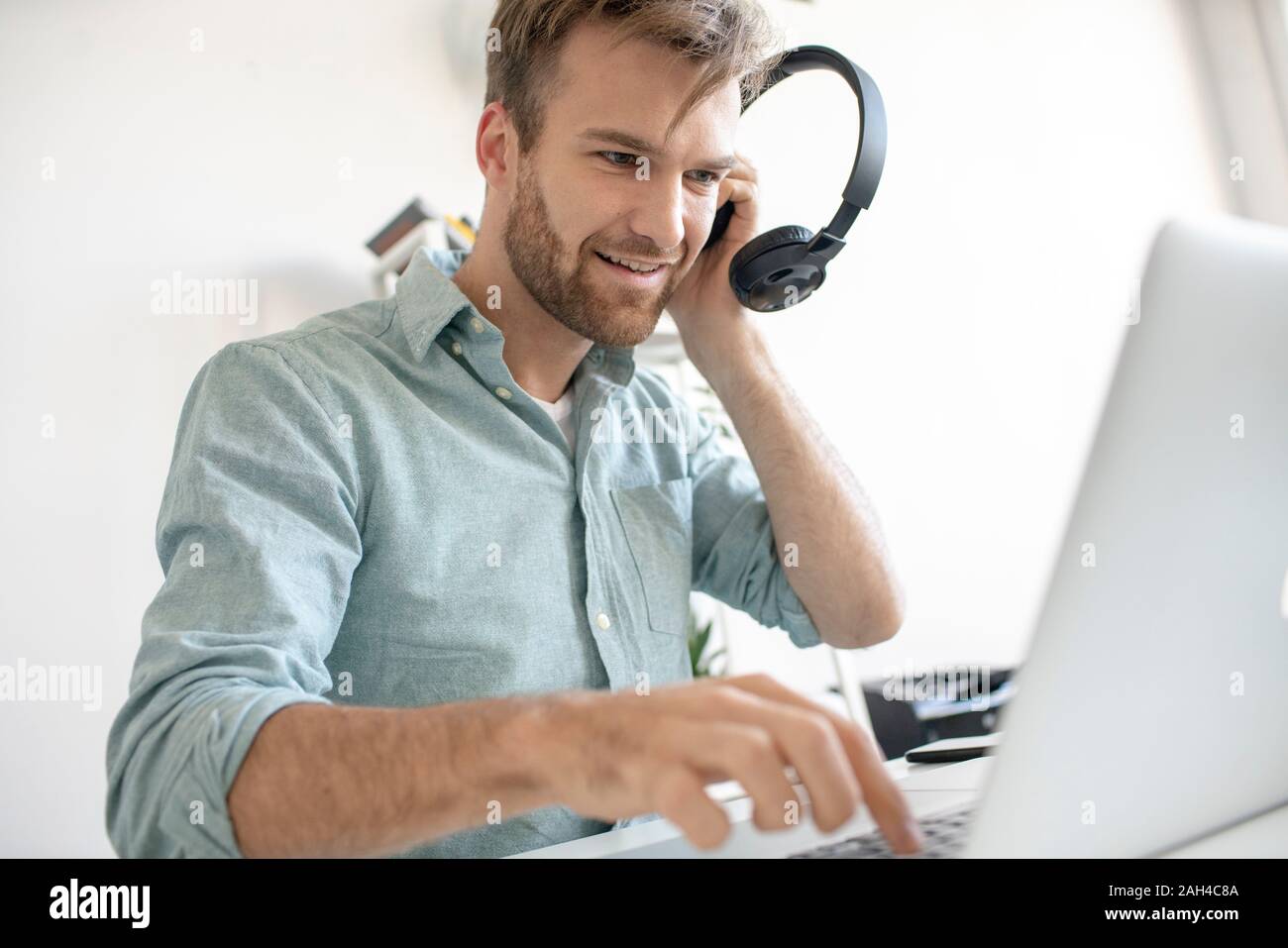 Lächelnder Mann mit Kopfhörer und Notebook am Schreibtisch im Büro Stockfoto