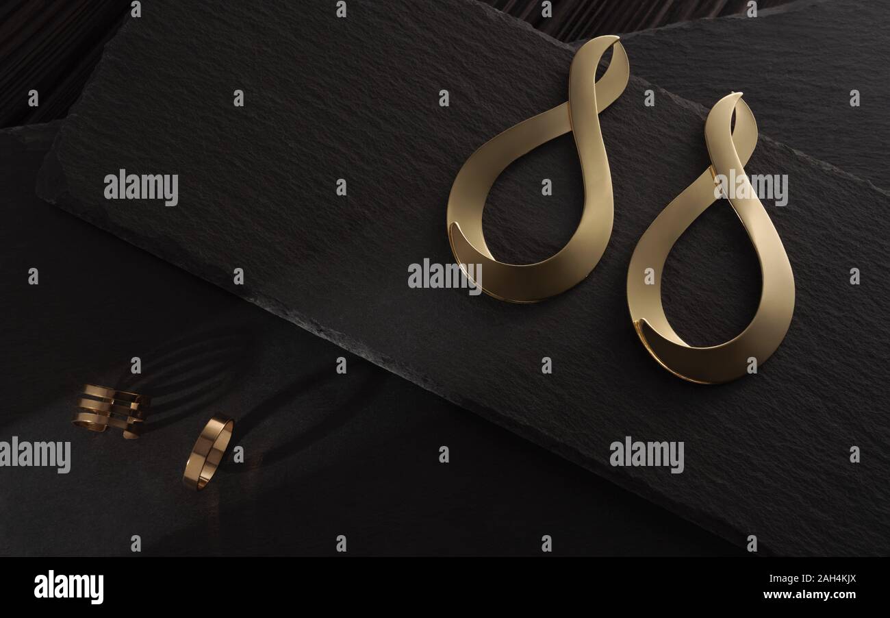 Sonnenlicht auf Moderne infinity Form gold Ohrringe und Ringe auf dunklem Stein Platten Stockfoto