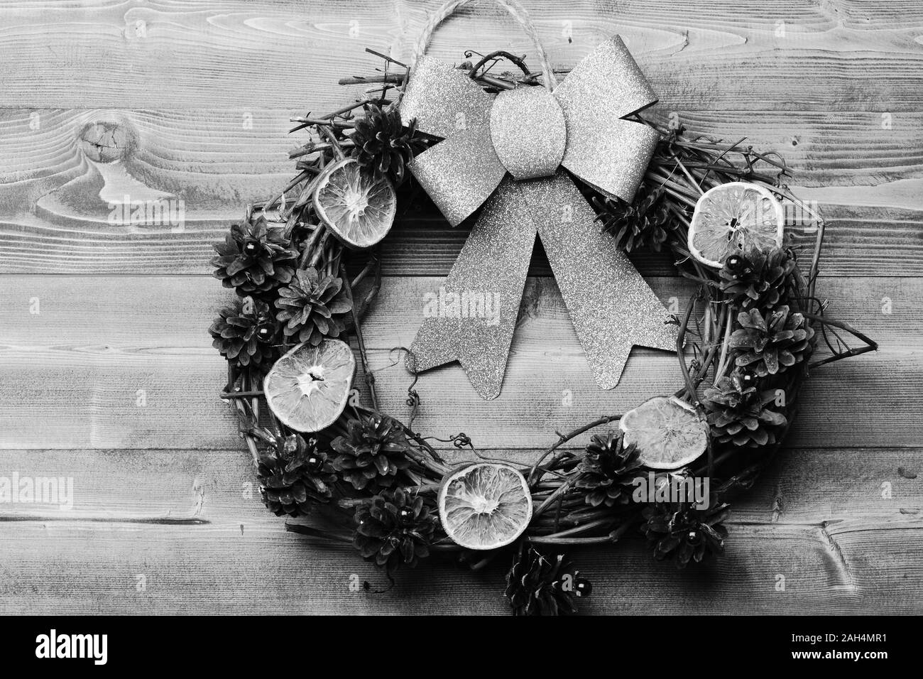 Eco Kranz und großen goldenen Bogen auf Holz- Hintergrund. Kranz aus Traubenmost Zweige mit trockenen Citrus Schichten und Tannenbaum Kegel. Weihnachtsdekoration mit organischen Spielzeug. Weihnachtsdekor Konzept. Stockfoto