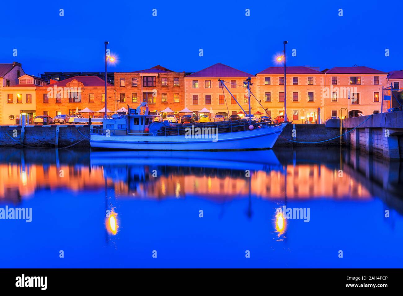 Hobart city Hafen Sullivans Cove bei Sonnenuntergang mit hell beleuchtete Küste von historischen Gebäuden entlang Pier mit Fischerboot in der Reflexion Stockfoto