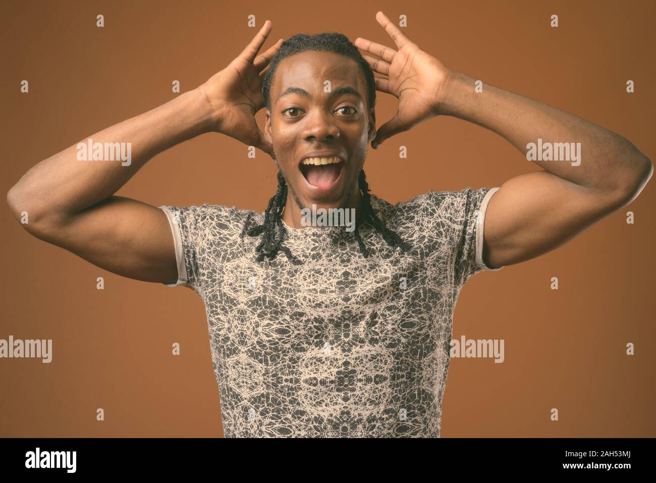 Studio shot der jungen schönen afrikanischen Mann mit grauen Hemd gegen braunen Hintergrund Stockfoto