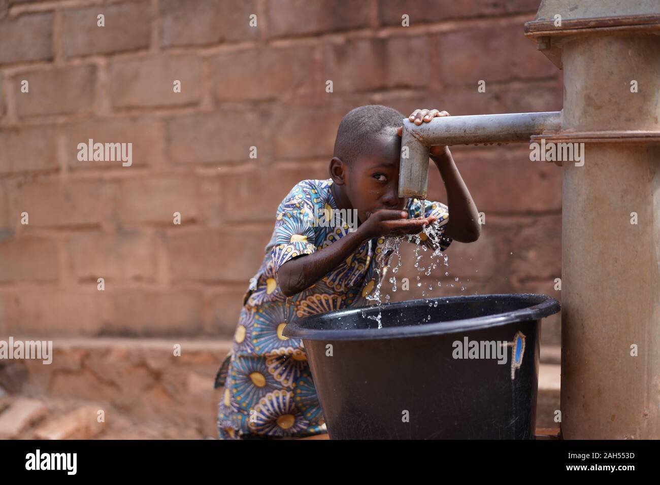 Little African Boy In Der Community Borehole Quenching Seinen Durst Stockfoto
