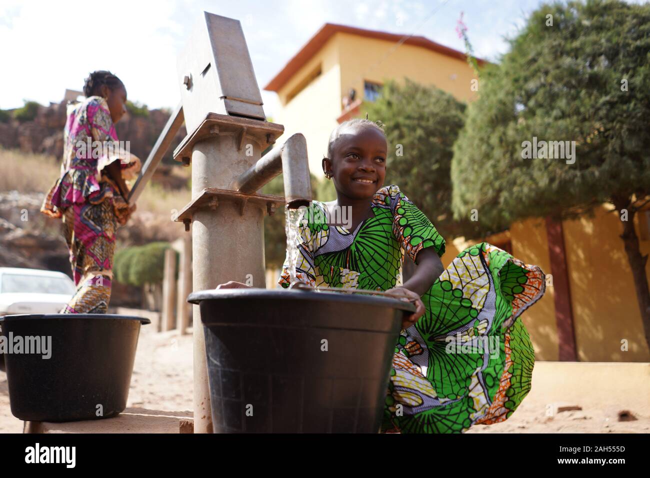 Zwei Bunt Gekleidete Afrikanische Mädchen, Die Wasser am Bohrloch Holen Stockfoto