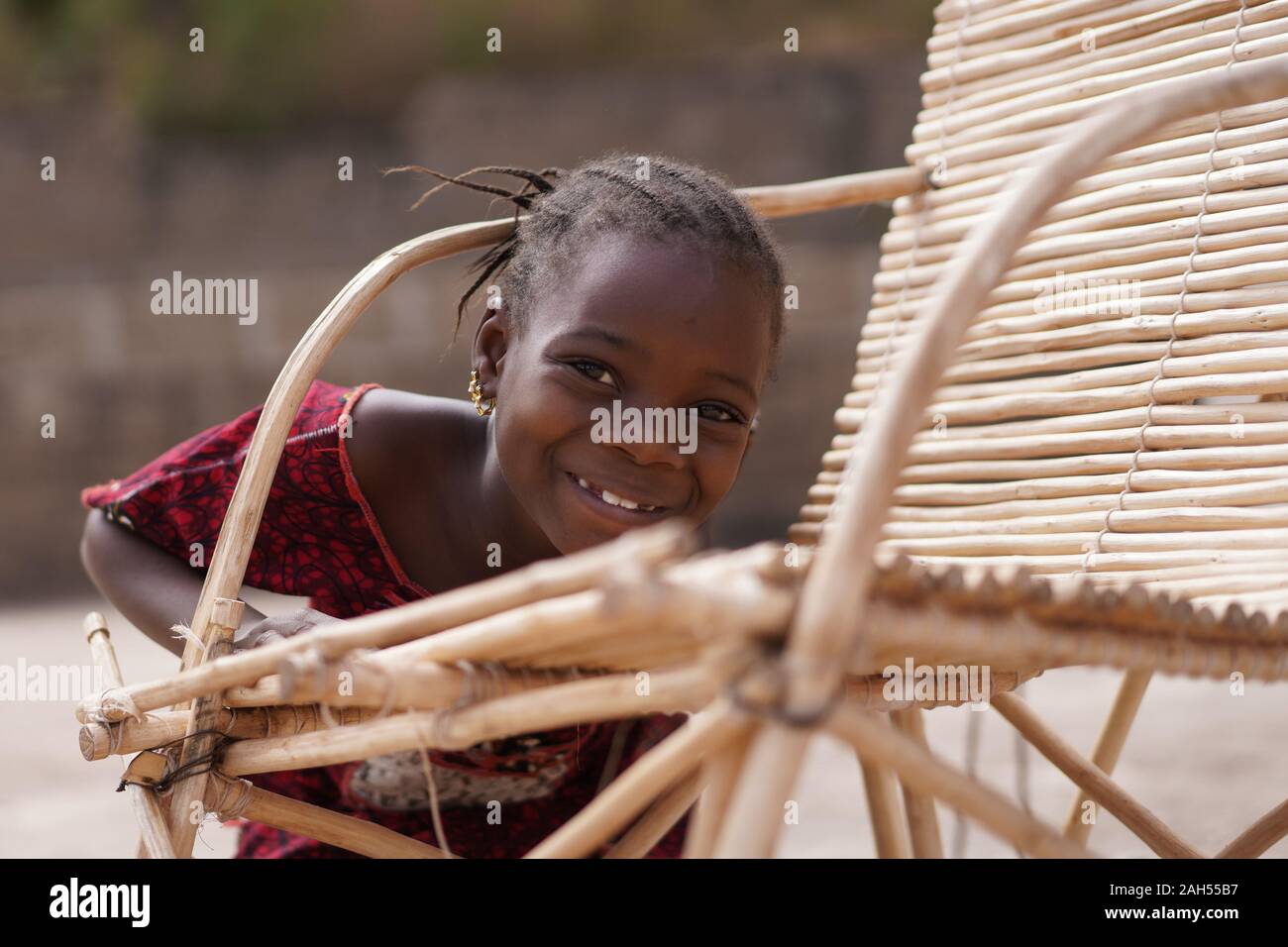 Cute afrikanisches Mädchen herum täuschen mit ihrem traditionellen Zuckerrohr Stuhl Stockfoto