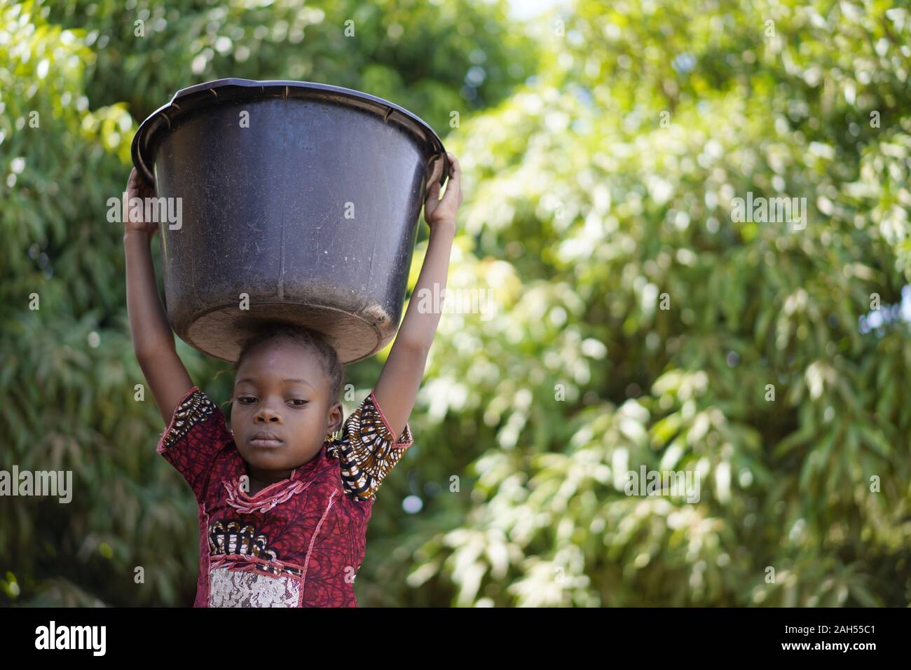 Gestörte kleine Afrikanische Mädchen, das versuchte zu einem schweren Wassereimer auf dem Kopf Stockfoto