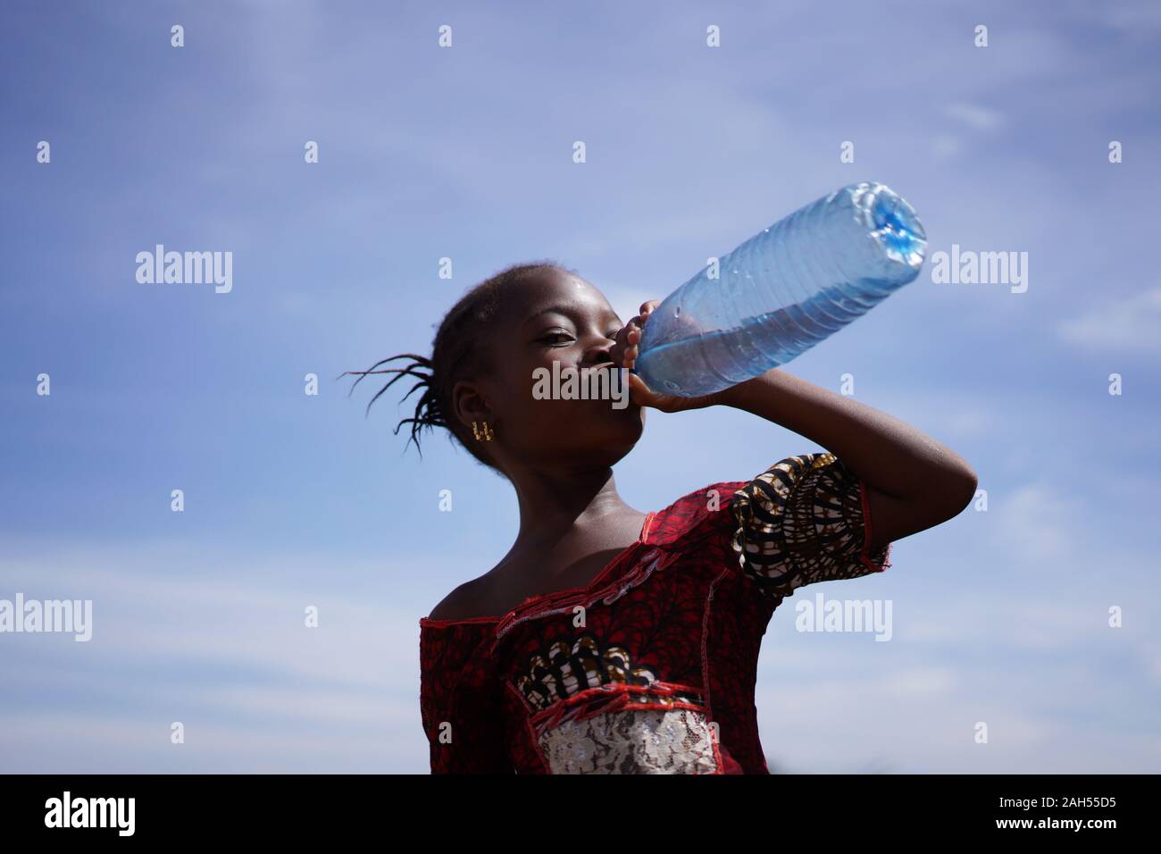 Afrikanisches Mädchen trinken aus einer Wasserflasche unter Ein intensiv blauen Himmel Stockfoto
