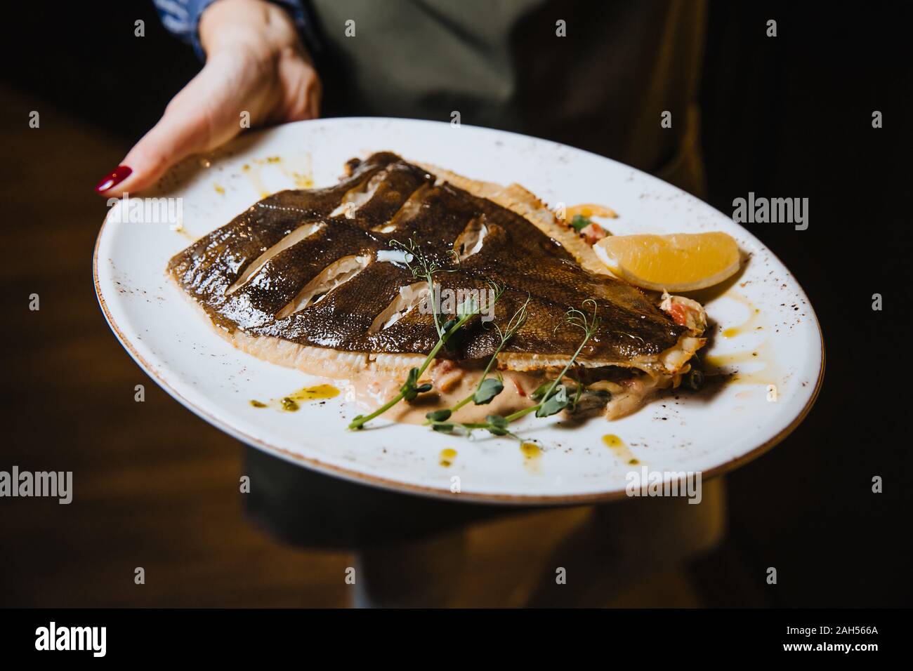Gebackener Fisch mit Zitrone liegt in einer runden Platte. Stockfoto