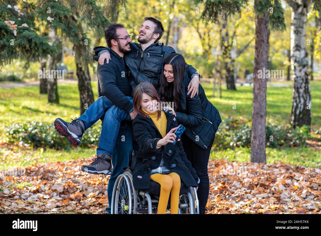 Junge behinderte Frau im Rollstuhl, die selfie mit Freunden in einem Park Stockfoto