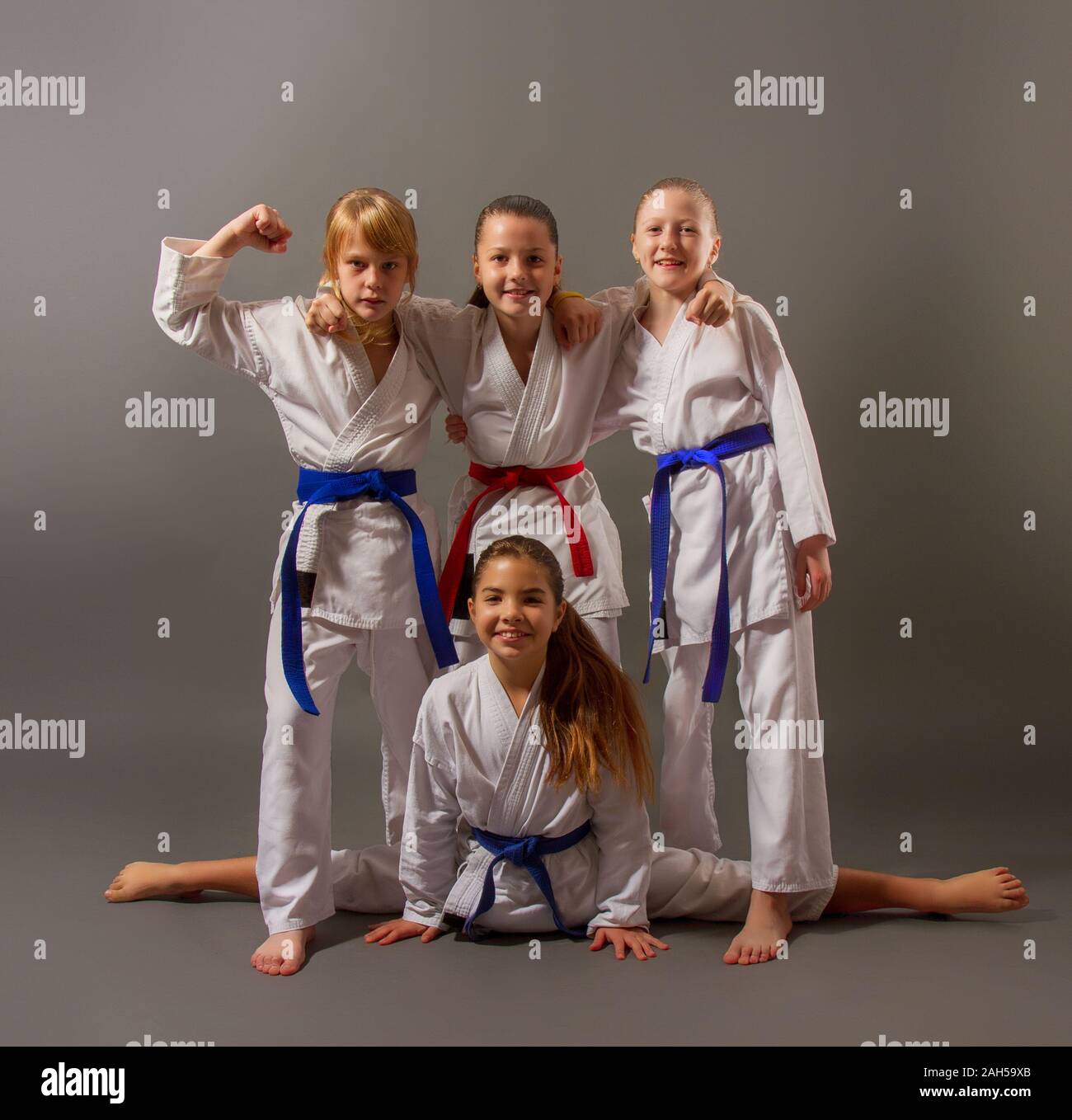 Vier kleine Karate Mädchen in weißen Kimonos auf einem dunklen Hintergrund gut gelaunt Posing Stockfoto
