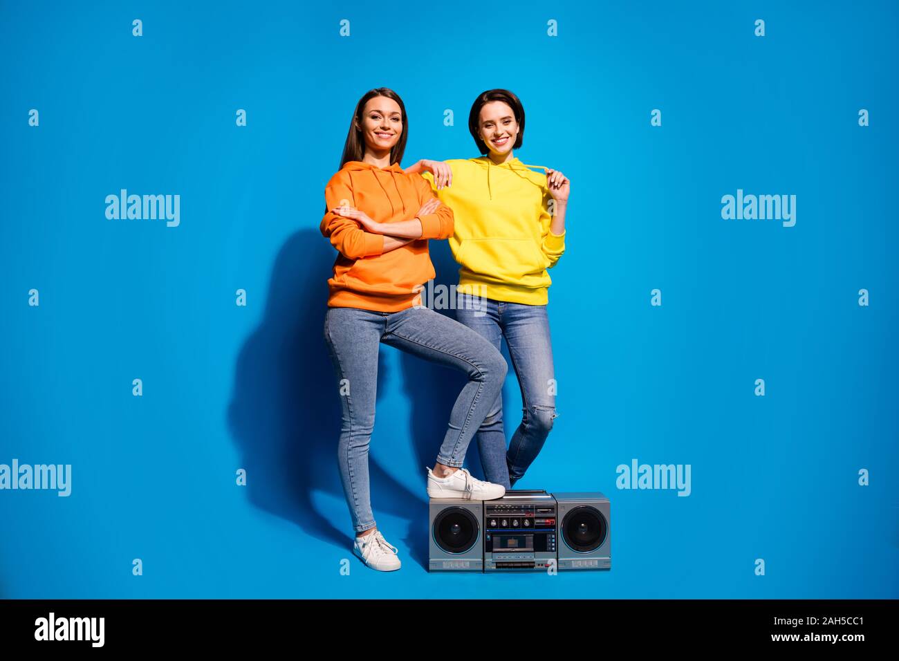 Voller Körper Foto von zwei Damen mit Vintage tape recorder zum Chillen Party mit modernen, Rhythmen tragen Casual orange gelb Hoodies isoliert Blau col Stockfoto