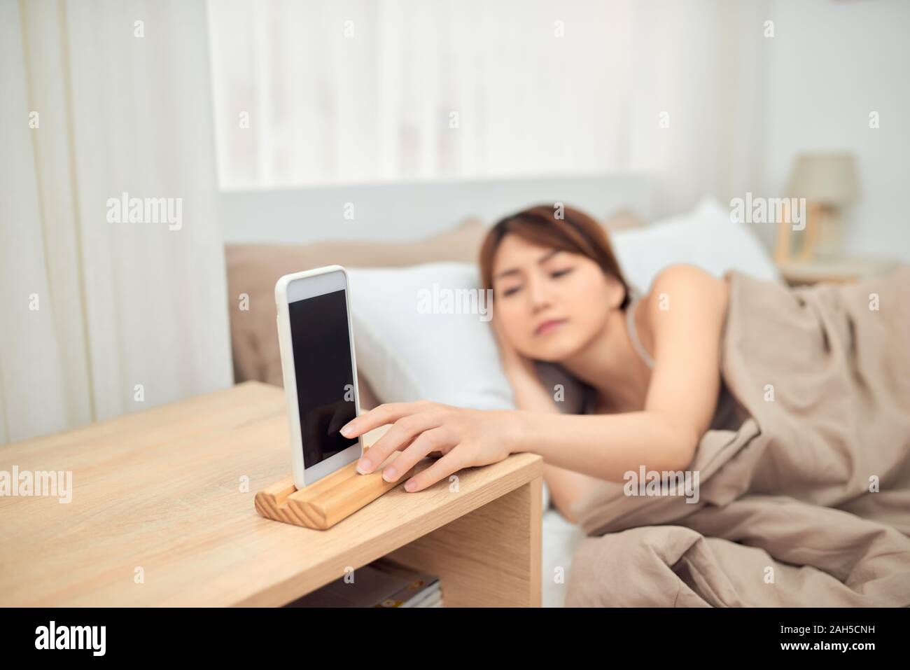 Ärgerlich Alarm. Frau im Bett liegend per Handy geweckt werden, das Ausschalten verrauschtes Signal, Nahaufnahme Stockfoto