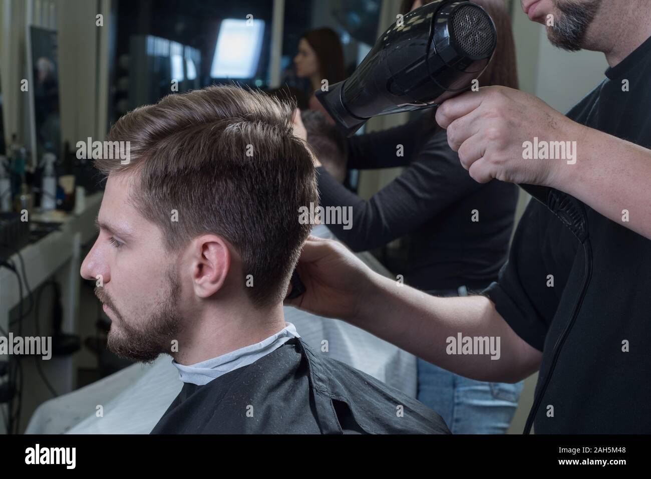 Close-up. Master Friseur blow-drys ein junger Kerl in einem Friseursalon. Pflege für Männerhaar. Männer Schönheit. Haarschnitt und Styling Stockfoto