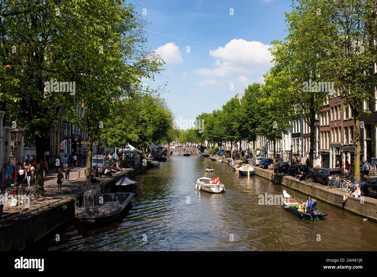 Blick auf Menschen, kleine Boote auf Kanal einer Mittelmeerkreuzfahrt tour in Amsterdam. Bewölkt blauer Himmel und Bäume werden auch in der Ansicht. Es ist ein sonniger Sommertag. Stockfoto