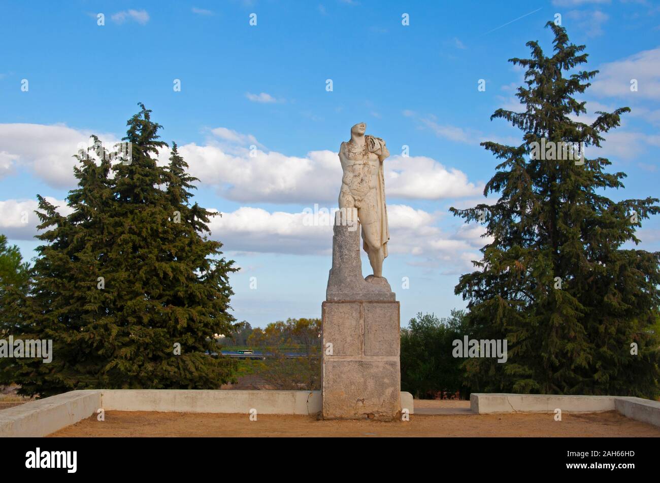 Antike Skulptur der Mann in der römischen Stadt Italica in Sevilla, Spanien. Grüne Bäume und blauer Himmel mit Wolken. Stockfoto