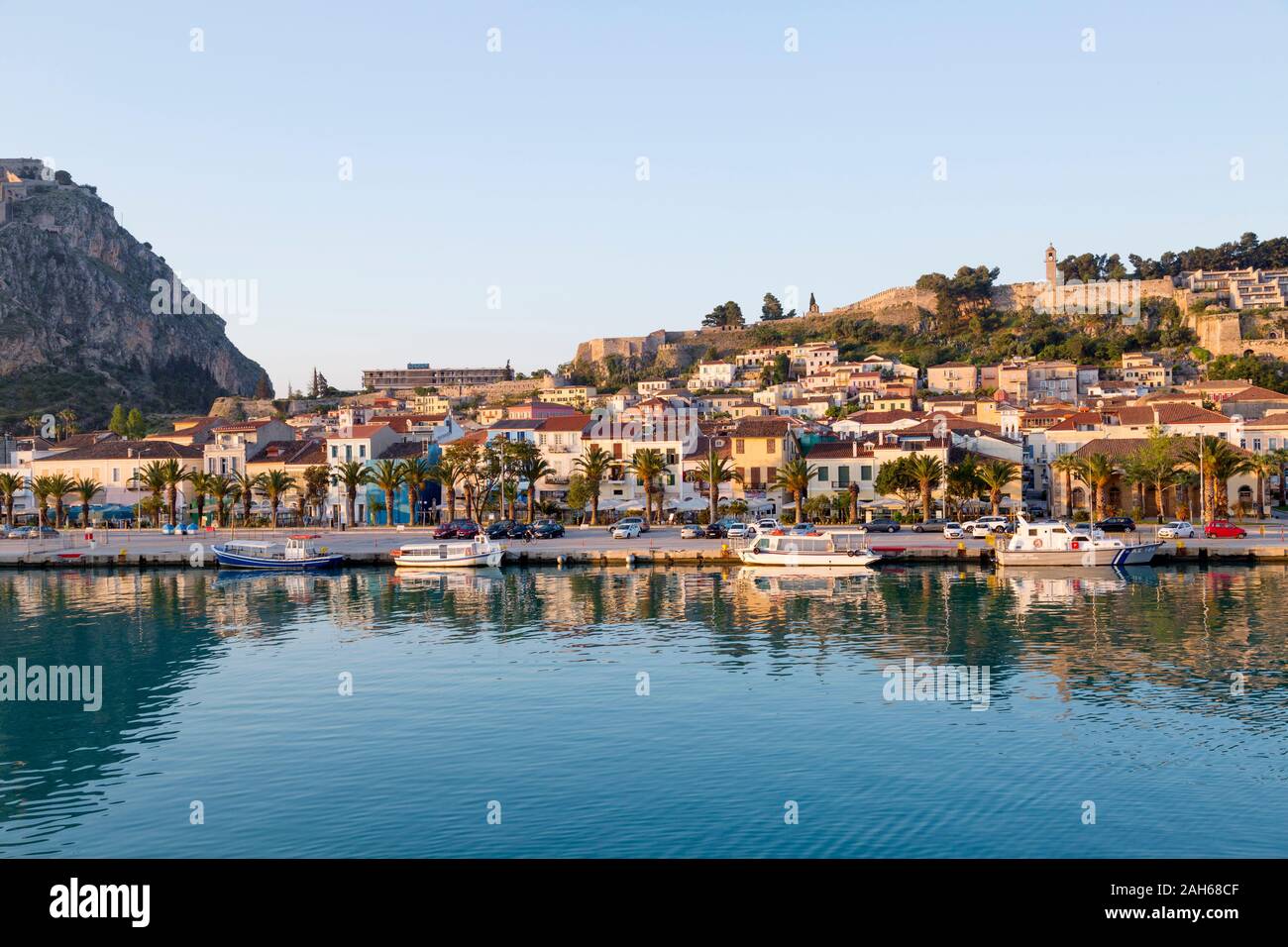 Anzeigen von Nafplio, mit seiner Reflexion in den ruhigen Gewässern der Hafen auf einer sonnigen Frühlingsmorgen, mit blauem Himmel. Die Festung Palamidi befindet sich auf der Spitze der Stadt. Stockfoto