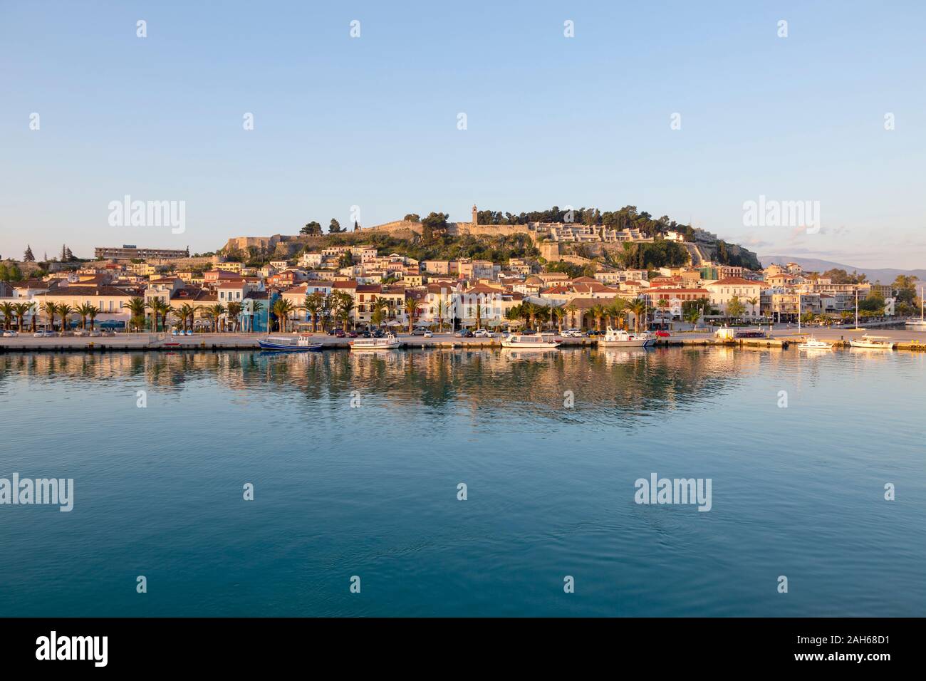 Anzeigen von Nafplio, mit seiner Reflexion in den ruhigen Gewässern der Hafen auf einer sonnigen Frühlingsmorgen, mit blauem Himmel. Die Festung Palamidi befindet sich auf der Spitze der Stadt. Stockfoto