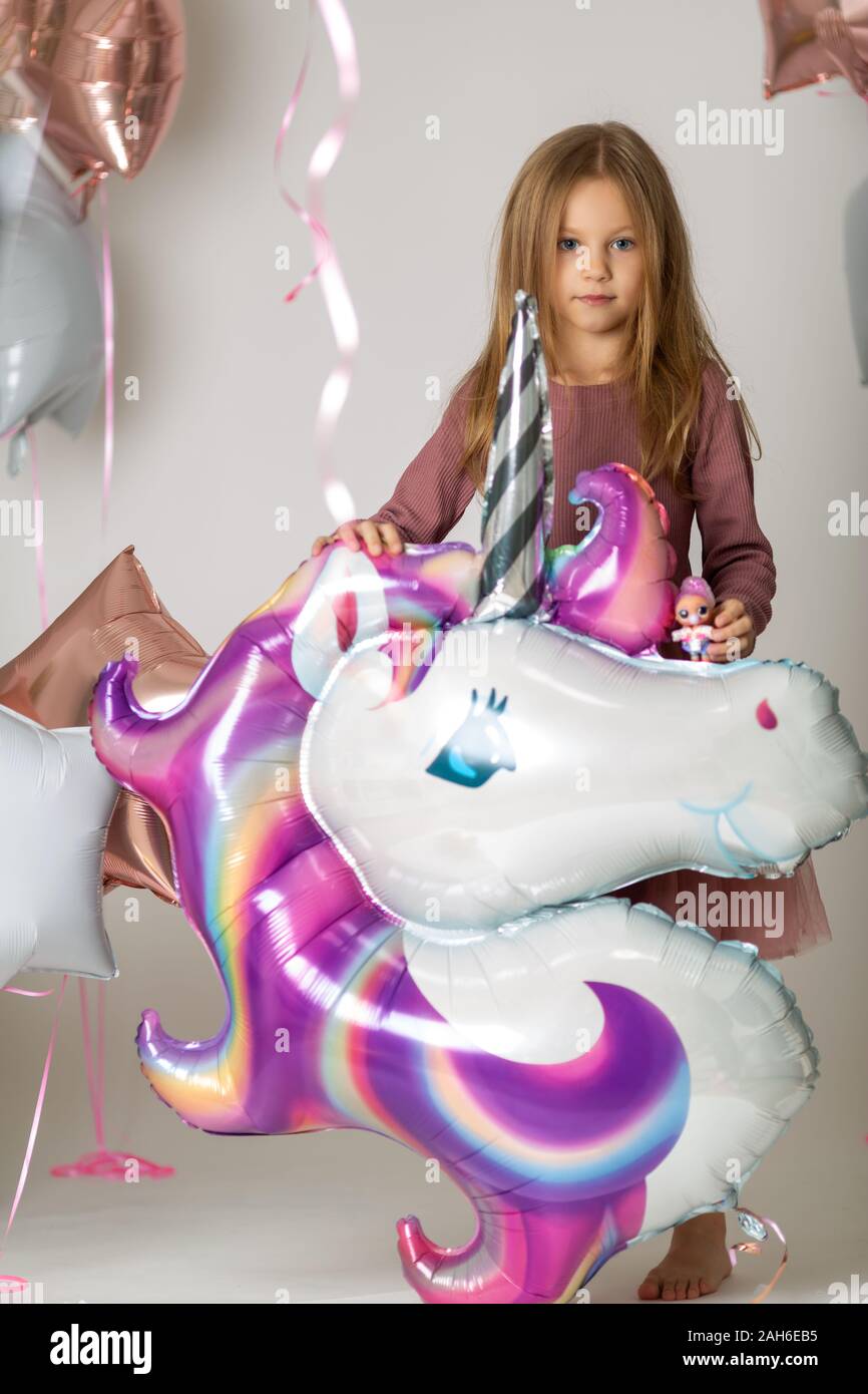 Blonde Mädchen mit blauen Augen in einem Kleid hat einen großen Helium Einhorn Kugel Stockfoto