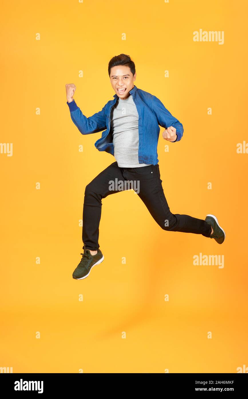 Junge glücklich Asian teen springen Willkommen auf Orange Studio Hintergrund isoliert Stockfoto