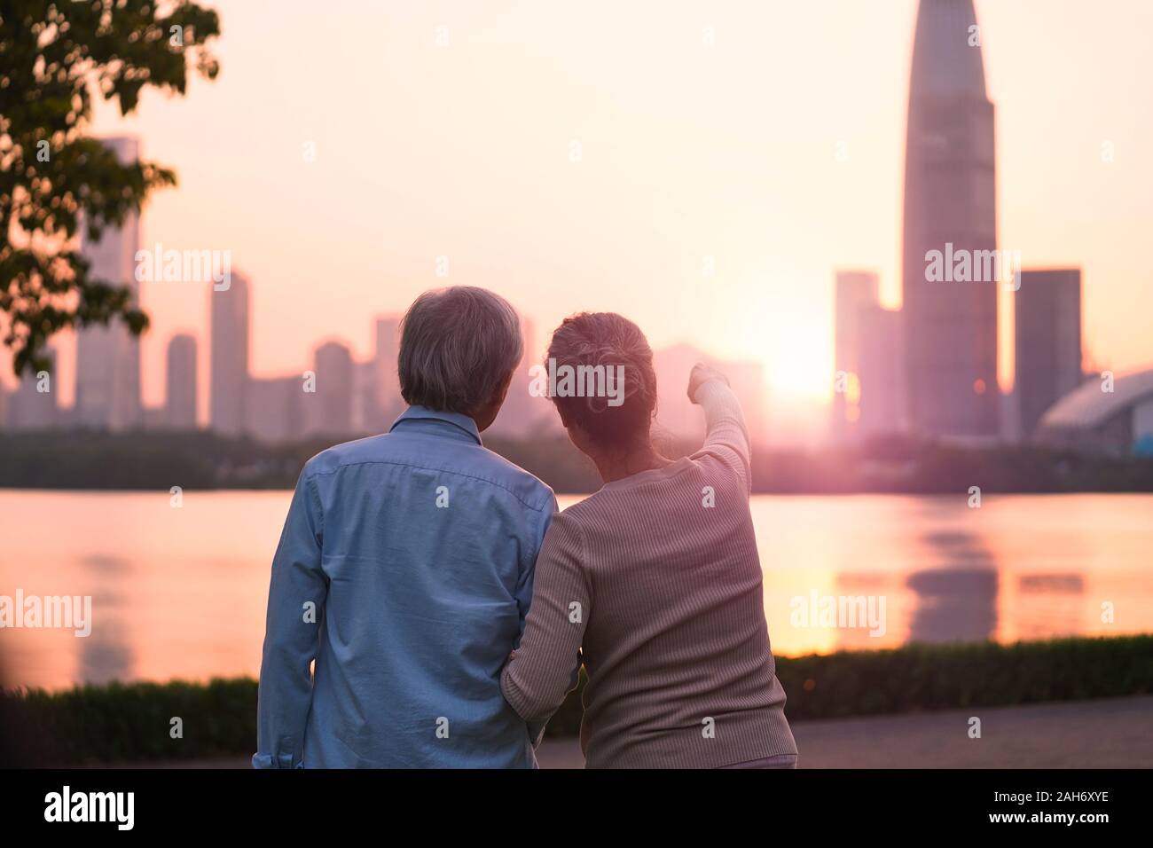 Ansicht der Rückseite des Älteren asiatischen Paar suchen bei Sonnenaufgang und die Skyline der Stadt vom Fluss Stockfoto
