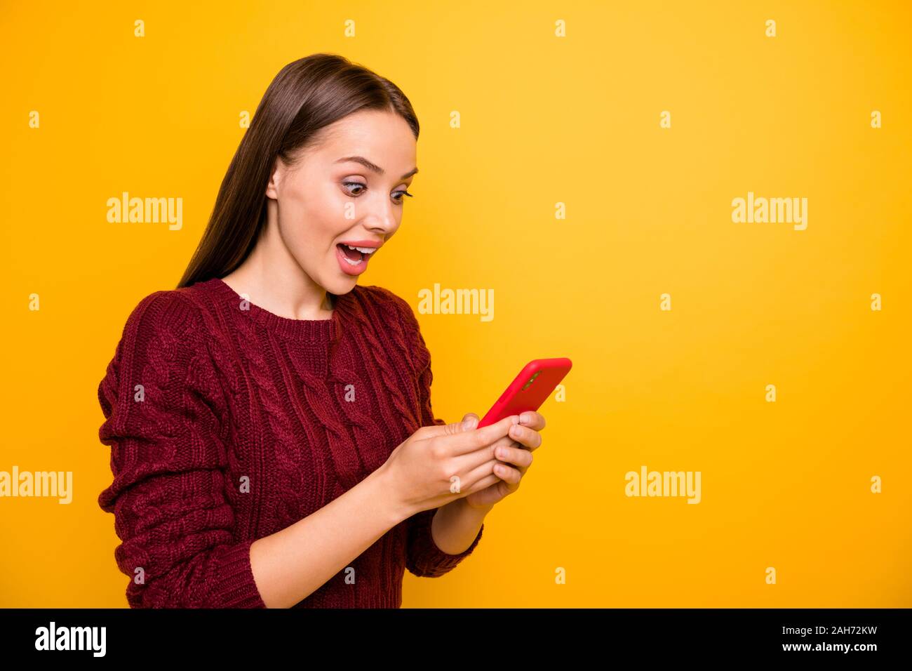 Turner Foto von beeindruckt cute tausendjährigen Holding moderne Technik, schreiende tragen maroon Pullover über Gelb Hintergrund isoliert Stockfoto