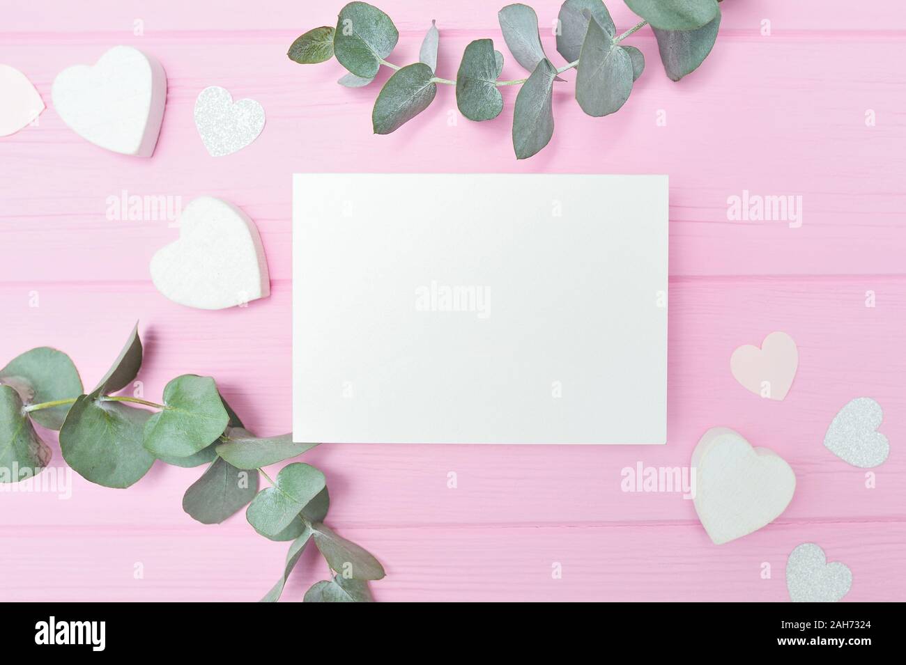 Valentines Tag oder Hochzeit mockup Szene mit leere Karte, Eukalyptus Blätter frame Papier Herzen Konfetti- und Holz- rosa Hintergrund, leeren Raum für Ihre Stockfoto