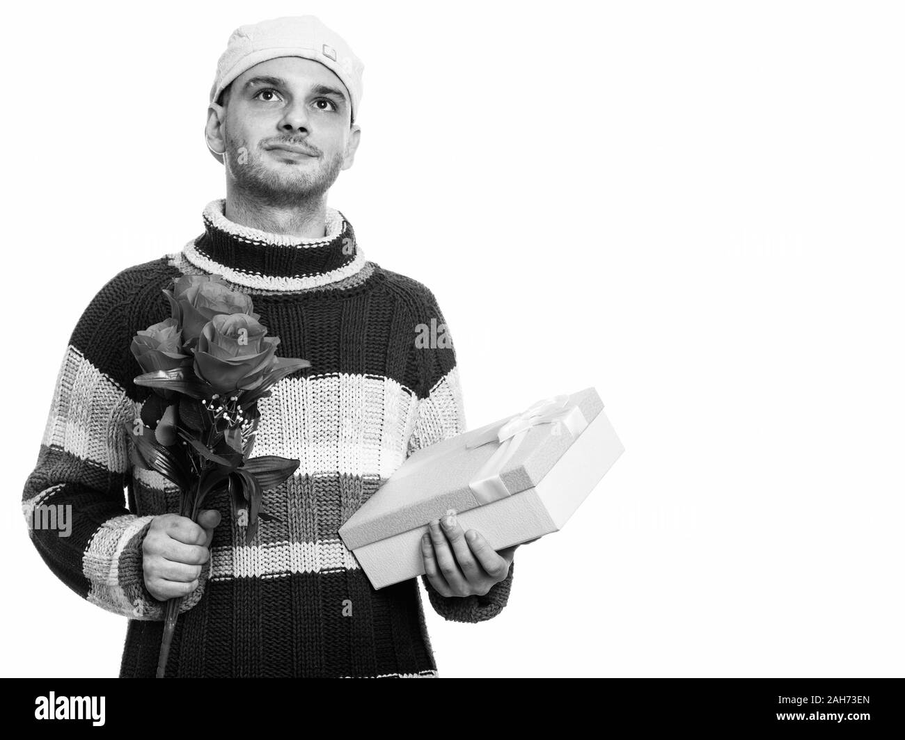 Studio shot junger Mann mit roten Rosen und Geschenkbox beim Denken Stockfoto