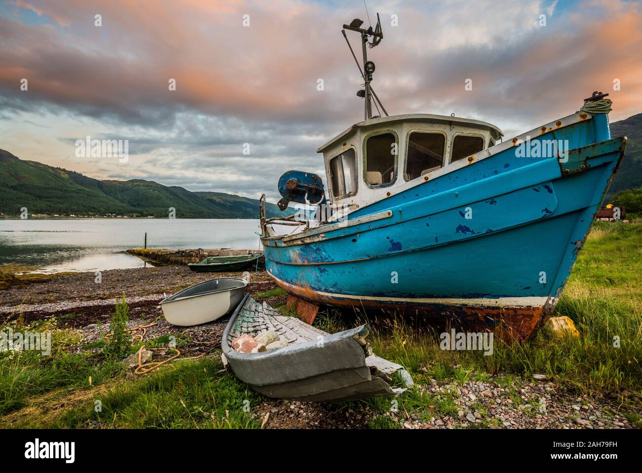 Sonnenaufgang auf einem abgelegenen schottischen See mit einem blauen Fischer Boot im Vordergrund und ferne Hügel im Hintergrund Stockfoto