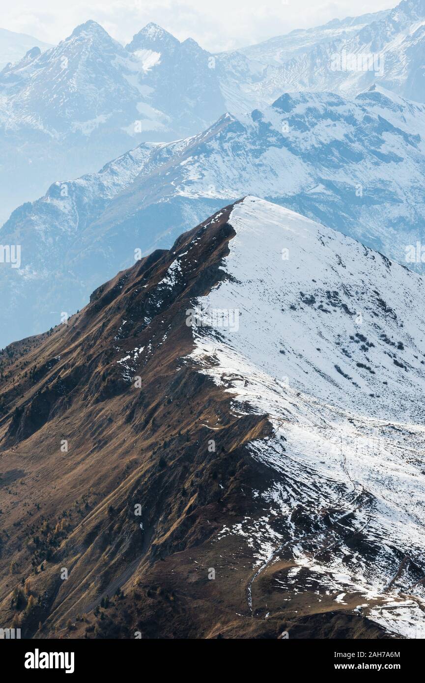 Nahaufnahme eines Bergkamms, der teilweise mit Schnee bedeckt ist, mit einer entfernten Bergkette im Hintergrund Stockfoto