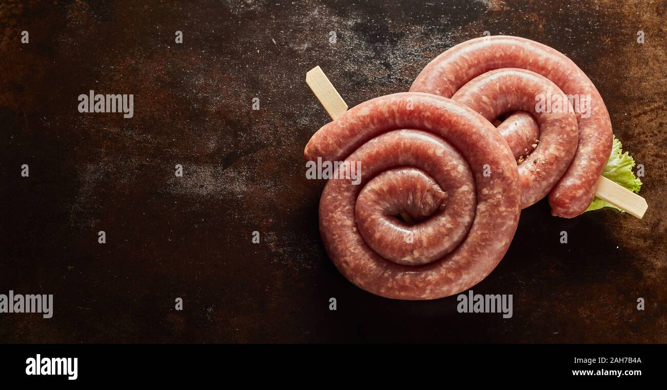 Zwei Spulen der würzigen Rohwurst in einem Panorama Banner über eine Dark Metal Bratpfanne Hintergrund zur Seite mit Kopie Raum für Werbung Stockfoto