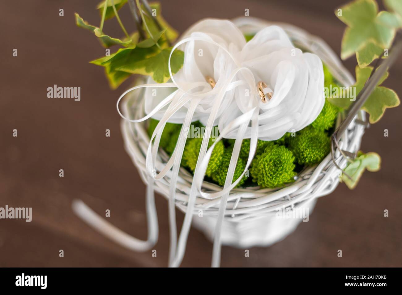 Zwei goldene Eheringe werden auf einem weißen Kissen gehalten Innen ein Korbkorb mit Efeu verziert Stockfoto