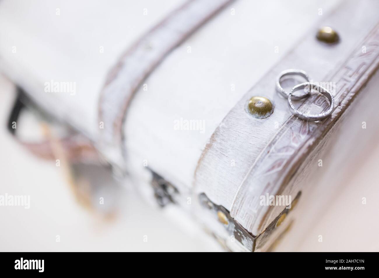 Zwei weißgoldene Eheringe, die auf einem verwitterten Weiß liegen Holzkiste vor einem Bokeh Hintergrund Stockfoto